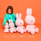 Child in Teal Sweater Sits with Four Pink Stuffed Bunnies of Increasing Sizes 23 Cm to 70 Cm Lined Up on an Orange Background