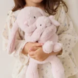 Child in a Floral Dress Holds a Fluffy Pastel pink Bunny Plush Toy Close to Their Chest