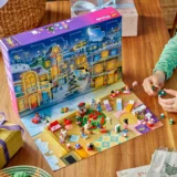 Lego Advent Calendar Opened on a Table Revealing Numbered Doors a Snowy Village Scene and Scattered Minifigures and Accessories on a Play Mat