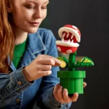 Person in a Denim Jacket Assembling a Lego Green Potted Plant with a Red Piranha Plant Figure and a Gold Coin in Hand
