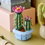 Two Lego Cactus Sculptures with Pink Flower Tops on a Light Blue Pedestal Displayed Beside Gift Boxes and a Potted Cactus