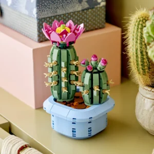 Two Lego Cactus Sculptures with Pink Flower Tops on a Light Blue Pedestal Displayed Beside Gift Boxes and a Potted Cactus
