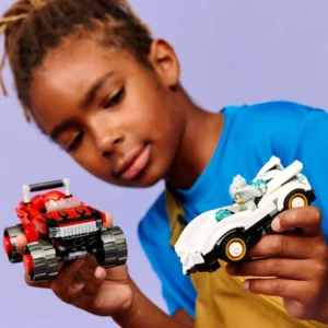 Child Playing with Two Lego style Toy Vehicles a Red Monster Truck in One Hand and a White Futuristic Car in the Other Against a Purple Background