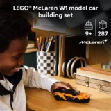 Child Smiling As They Play with an Orange Lego Mclaren W1 Model Car on a Wooden Desk