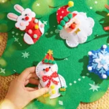 Hand Places a White Felt Snowman Ornament with a Red Bow on a Green Christmas Scene with a Santa and Blue Snowflake Decorations Nearby