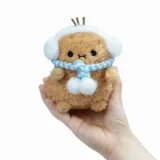 Small Brown Plush Toy Wearing White Earmuffs and a Blue Scarf Held in a Hand