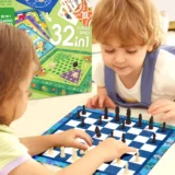 Two Children Sit at a Table Playing Chess on a Blue and White Board with a Colorful Game Box in the Background