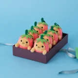 Pink Strawberry Plush Toys with Green Leaves in a Purple Gift Box on a Blue Background