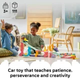 Two Children Play with a Colorful Car on a track Construction Set on the Living Room Floor Smiling and Building Together