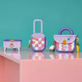Three Pastel Purple Toy Bags with Multicolor Circular Patterns Displayed on a Glossy Pink Surface Against a Teal Background a Small Chest a Suitcase and a Handbag