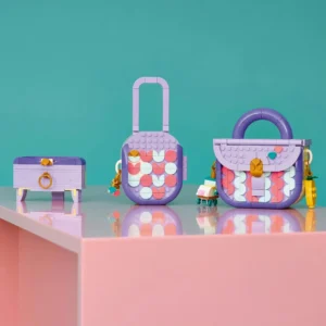 Three Pastel Purple Toy Bags with Multicolor Circular Patterns Displayed on a Glossy Pink Surface Against a Teal Background a Small Chest a Suitcase and a Handbag