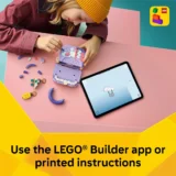 Child Wearing a Yellow Knit Hat Builds a Purple Lego Set at a Pink Desk Tablet Shows Lego Builder App Instructions