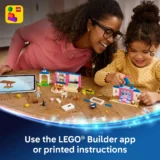 Two Women and a Young Girl Build Lego Sets at a Wooden Table Using a Tablet for Instructions and Colorful Bricks Scattered Around