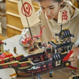 Young Person Assembling a Large Black and red Lego Pirate Ship Fortress with Banners on a Table Surface