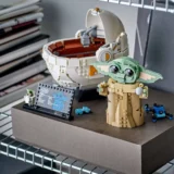 Lego Scene with Grogu baby Yoda Figure Beside a Large White Circular Pod and a Small Blue Droid on a Display Base