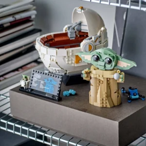 Lego Scene with Grogu baby Yoda Figure Beside a Large White Circular Pod and a Small Blue Droid on a Display Base